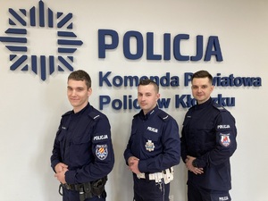trzech policjantów stoi obok siebie w sali sztabowej , na ścianie napis Komenda powiatowa Policji w Kłodzku i logo policji