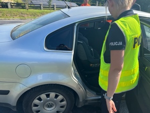policjantka stoi przy samochodzie osobowym w którym znajduje sie fotelik ochronny dla dzieci