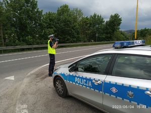 policjant stoi pryz radiowozie , na poboczu drogi zaparkowany radiowóz policyjny