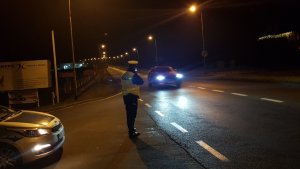 Policjant wydziału ruchu drogowego stoi przy radiowozie i mierzy prędkość nienadjeżdżającego samochodu osobowego.Zdjęcie wykonane w porze nocnej