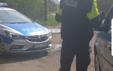 Policjant stoi przy samochodzie osobowym w tle widać radiowóz