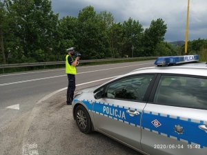 Policjant stoi na drodze , obok zaparkowany radiowóz