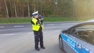 Policjant z miernikiem prędkości stoi na drodze przy radiowozie