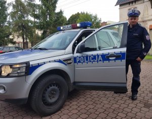 policjant stoi przy radiowozie policyjnym na placu