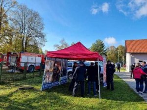 policjant i policjantka znajdują sie w namiocie policyjnym przy stoliku na którym są materiały prewencyjne obok stoją uczestnicy festynu , zdjęcie wykonane na świeżym powietrzu