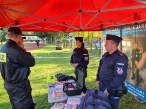 policjant i policjantka znajdują sie w namiocie policyjnym na świeżym powietrzuprzy stoliku na którymn są materiały prewencyjne obok stoi męzcyzna