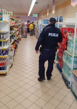 policjant w mundurze idzie na terenie placówki handlowej,obok widać regał z artykułami spożywczymi