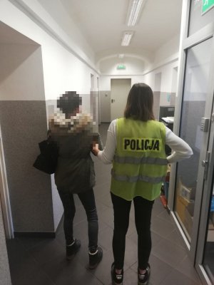 policjant prowadzi zatrzymaną kobietę w pomieszczeniu służbowym