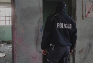 policjant idzie przez teren pustostanu, na ziemi leża śmieci