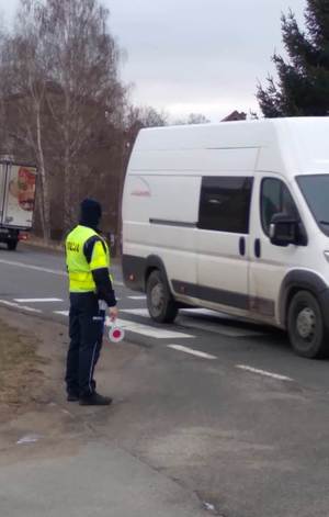 policjant stoi przy przejściu dla pieszych , jadą samochody po jezdni