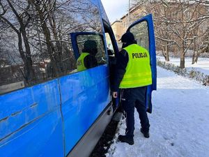 Policjant stoi pryz busie i prowadzi kontrole, na drodze leży śnieg