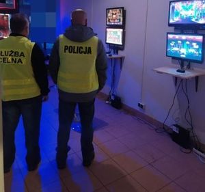 policjant i celnik w kamizelkach z napisami na plecach policja i służba celna stoją przy automatach w pomieszczeniu