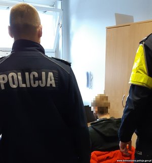 dwóch policjantów stoi przy zatrzymanym w pomieszczeniu służbowym