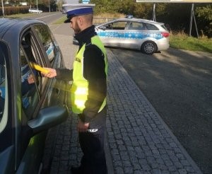 policjant stoi przy samochodzie i sprawdza stan trzeźwości kierującego