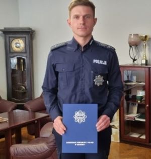 policjant w mundurze trzyma w ręku obwolutę  papierową