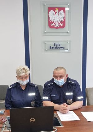 policjantka  i policjant siedzą przy komputerze, za nimi na ścianie napis sala sztabowa oraz umieszczone godło państwowe