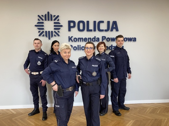 grupa policjantów stoi przy napisie Komenda Powiatowa Policji w Kłodzku, zdjęcie wykonane w pomieszczeniu