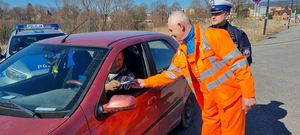 mężczyźni w kamizelkach wręczają upominek kierującemu autem