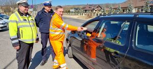 mężczyźni w kamizeleczkach oraz policjant stoją przy samochodzie osobowym