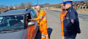 mężczyźni w kamizelkach odblaskowych oraz policjant  stoją przy samochodzie osobowym