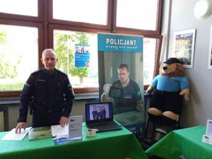 trzech policjantów znajduje sie w pomieszczeniu przy stole na którym znajduje sie laptop, a obok maskotka policyjna komisarz lew