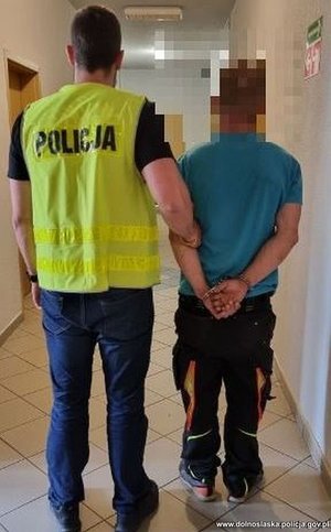 policjant w kamizelce z napisem policja prowadzi zatrzymanego mężczynę