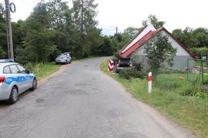 Po lewej stronie drogi stoją dwa radiowozy. Po lewej stronie drogi widoczny jest samochód osobowy, który uderzył w ścianę budynku mieszkalnego.