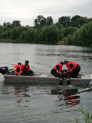 Policjanci, strażacy i woprowcy ćwiczą podejmowanie tonącego na łódkę.