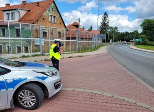 policjant stoi na drodze przy radiowozie z miernikiem prędkości w ręku