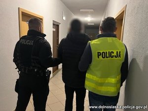 dwóch policjantów prowadzi zatrzymanego mężczyznę przez korytarz