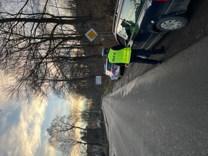 dwóch policjantów  na drodze prowadzi kontrole drogową , na zdjęciu samochód osobowy w tle ulica i radiowóz zaparkowsny na poboczu