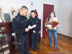 policjant i policjantka czytają list obok stoi kobieta z kwiatami w ręku