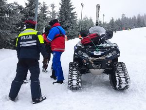 Na ośnieżonym stoku przy quadzie stoi policjant i ratownik gopr