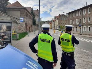 dwóch policjantów stoi przy radiowozie  w tle widać budynek