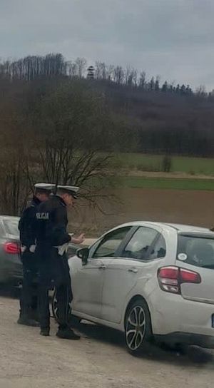 dwóch policjantów stoi przy aucie i prowadzi kontrole drogową