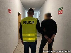 policjant prowadzi zatrzymanego mężczyznę przez korytarz komendy