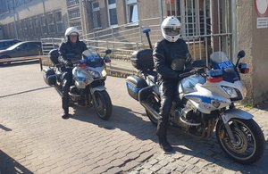 dwóch policjantów siedzi na motocyklach przy budynku komendy