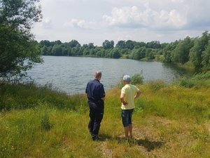 dwóch mężczyzn stoi obok siebie w tym jeden w mundurze policyjnym, widać wodę i drzewa