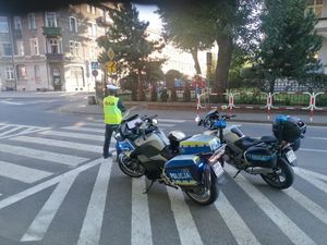 Policjant w mundurze stoi przy jezdni obok dwa policyjne motocykle