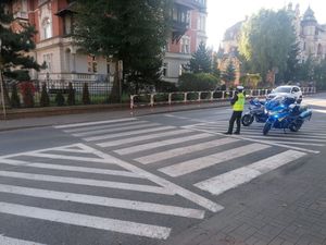 Policjant w mundurze stoi przy przejściu dla pieszych obok dwa motocykle policyjne