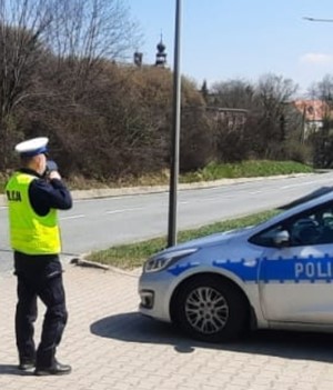 policjant z miernikiem prędkości w rękach stoi przy radiowozie na poboczu drogi