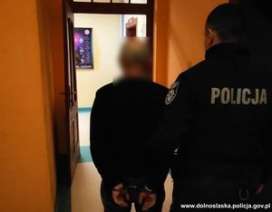 policjant prowadzi zatrzymanego meżczyzne, który ma kajdanki na rękach