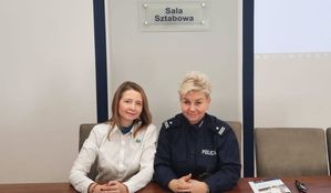policjantka w mundurze i kobieta w białej koszuli siedzą obok siebie przy komputerze w sali sztabowej