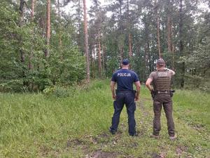 policjant i strażnik leśny w mundurach służbowych stoją przodem w tle widać las