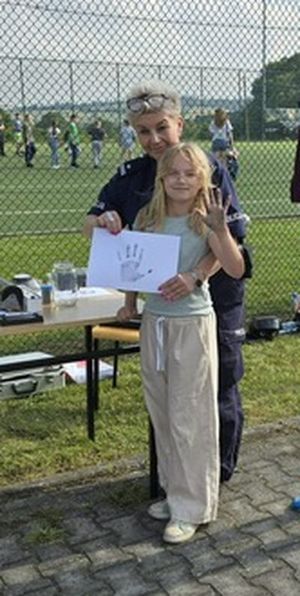 policjantka stoi z dziewczynka ,która pokazuje kartkę papieru z odbiciem ręki