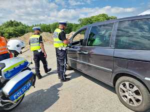 policjanci i przedstawiciele służb drogowych stoją przy samochodzie