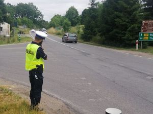 policjant stoi na poboczu drogi z miernikiem prędkości, widać jadące samochody