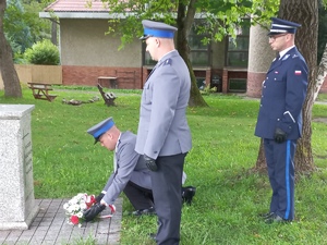 Zdjęcie z uroczystości święta Policji, złożenie wiązanki przy obelisku w ogrodach Ojców Franciszkanów w Kłodzku -policjant składa wiązanke