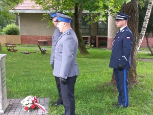 Zdjęcie z uroczystości święta Policji, złożenie wiązanki przy obelisku w ogrodach Ojców Franciszkanów w Kłodzku -policjanci stoją przy obelisku