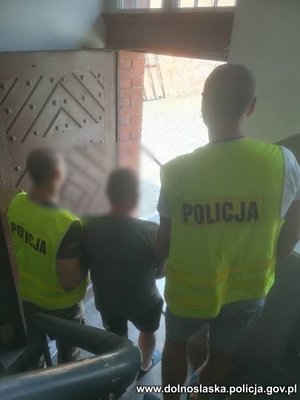 dwóch policjantów prowadzi zatrzymanego idą po schodach w kierunku drzwi